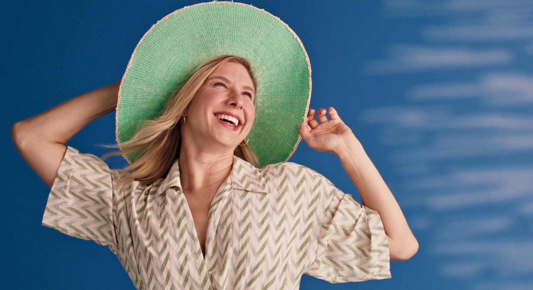 Dani Faitelson smiling in a green sunhat against a blue background